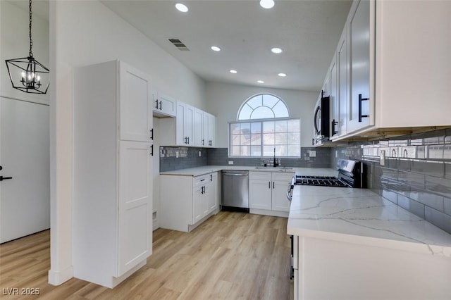 kitchen featuring appliances with stainless steel finishes, pendant lighting, lofted ceiling, white cabinets, and light stone countertops