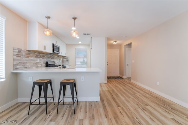 kitchen featuring a breakfast bar, white cabinetry, hanging light fixtures, decorative backsplash, and kitchen peninsula