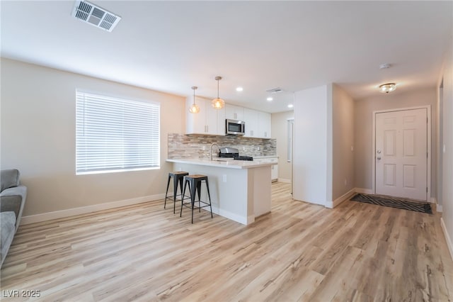 kitchen featuring appliances with stainless steel finishes, white cabinetry, tasteful backsplash, a kitchen bar, and kitchen peninsula