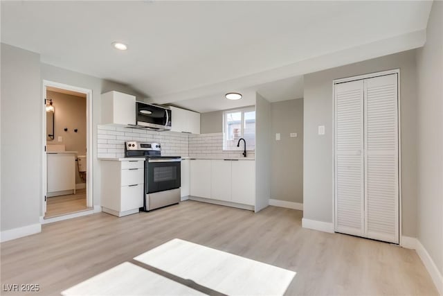 kitchen featuring appliances with stainless steel finishes, tasteful backsplash, sink, white cabinets, and light hardwood / wood-style flooring