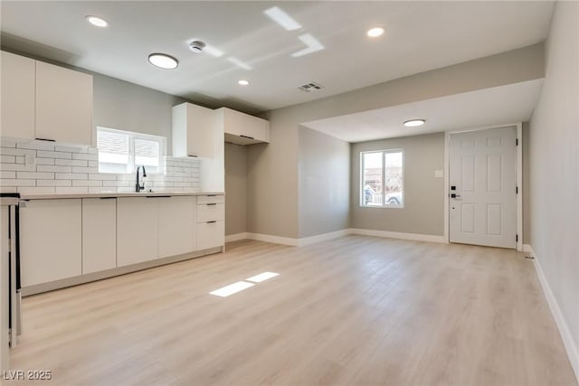 kitchen featuring white cabinetry, sink, light wood-type flooring, and backsplash