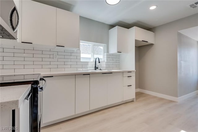 kitchen featuring electric range oven, white cabinetry, sink, decorative backsplash, and light hardwood / wood-style floors