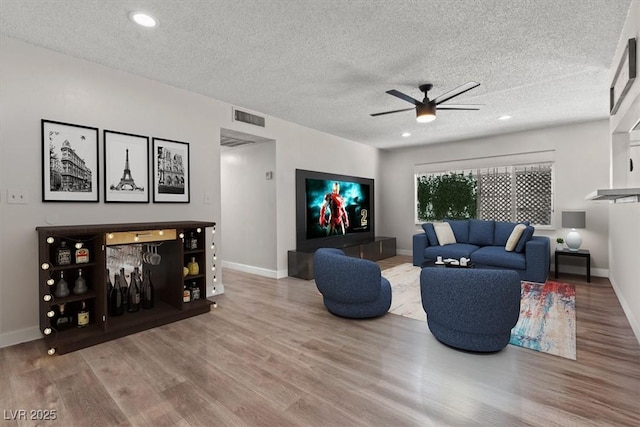 living room with baseboards, visible vents, ceiling fan, wood finished floors, and a textured ceiling