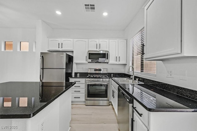 kitchen with stainless steel appliances, sink, white cabinets, and dark stone counters