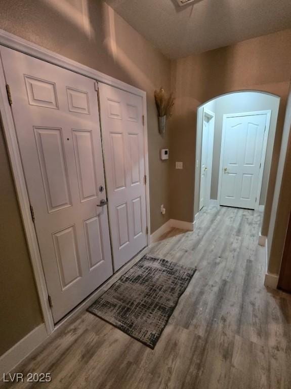 interior space featuring arched walkways, light wood finished floors, and baseboards