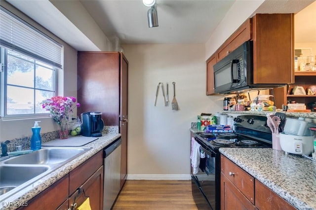 kitchen with sink, light hardwood / wood-style flooring, light stone counters, and black appliances