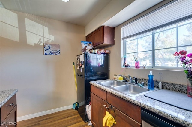 kitchen featuring dishwasher, sink, black refrigerator, and light wood-type flooring