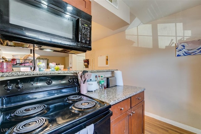 kitchen with light stone counters, light hardwood / wood-style flooring, black appliances, and vaulted ceiling