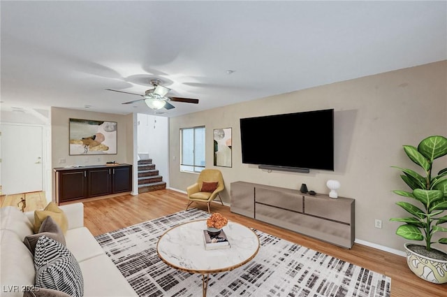 living area featuring light wood finished floors, baseboards, stairway, and a ceiling fan