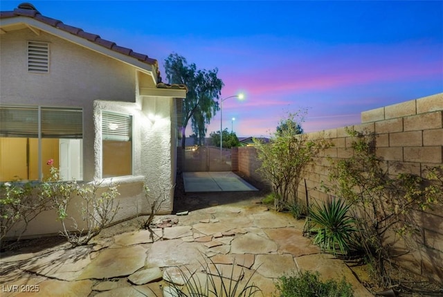 property exterior at dusk featuring stucco siding, a patio, a fenced backyard, and a tile roof