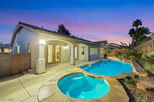 back of house at dusk featuring a fenced in pool, a fenced backyard, stucco siding, french doors, and a patio area