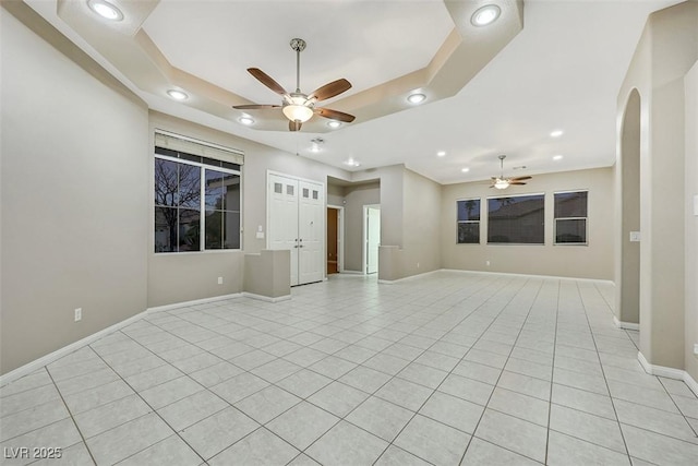 tiled empty room with a raised ceiling and ceiling fan