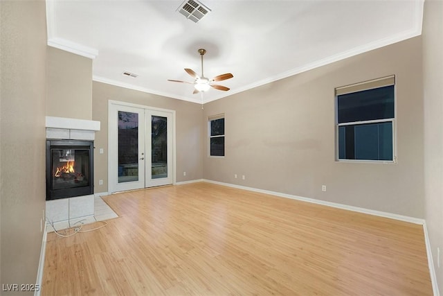 unfurnished living room featuring ceiling fan, a multi sided fireplace, ornamental molding, french doors, and light wood-type flooring