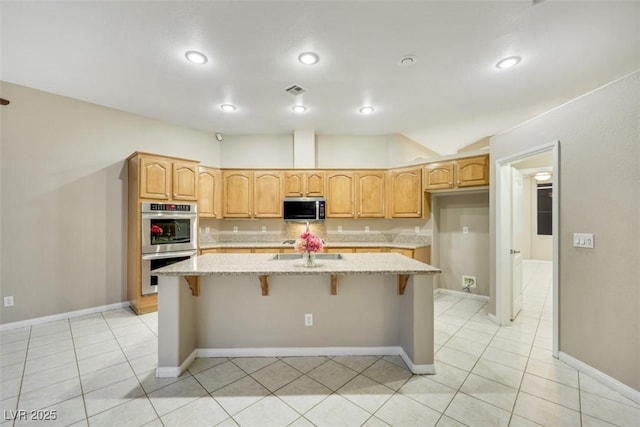 kitchen featuring light tile patterned floors, light stone counters, a kitchen island with sink, and appliances with stainless steel finishes