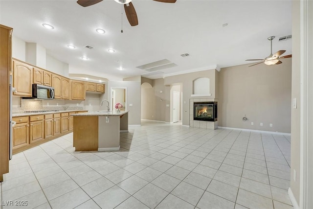 kitchen with sink, light tile patterned floors, a fireplace, a kitchen island with sink, and decorative backsplash