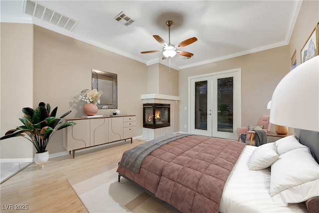 bedroom with visible vents, ornamental molding, a tiled fireplace, access to outside, and light wood-style floors