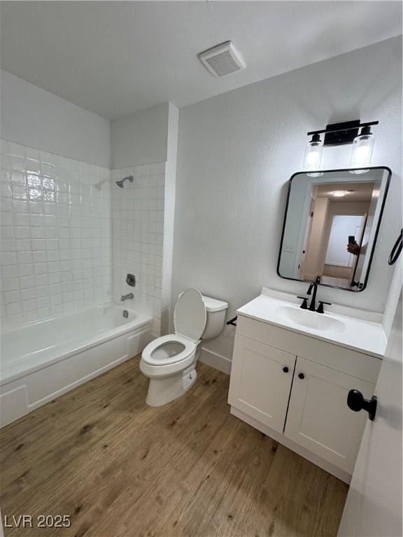 full bathroom with toilet, hardwood / wood-style flooring, tiled shower / bath combo, and vanity