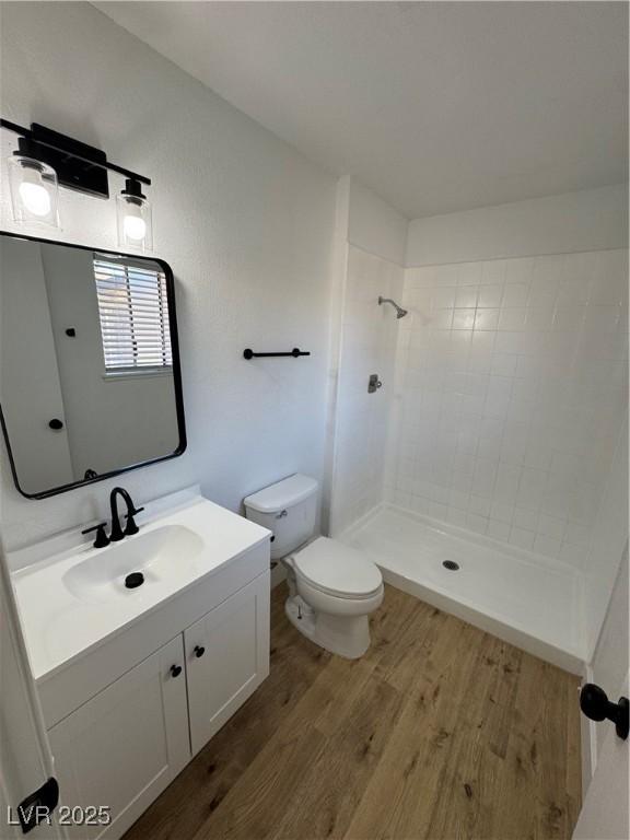 bathroom featuring toilet, vanity, tiled shower, and wood-type flooring