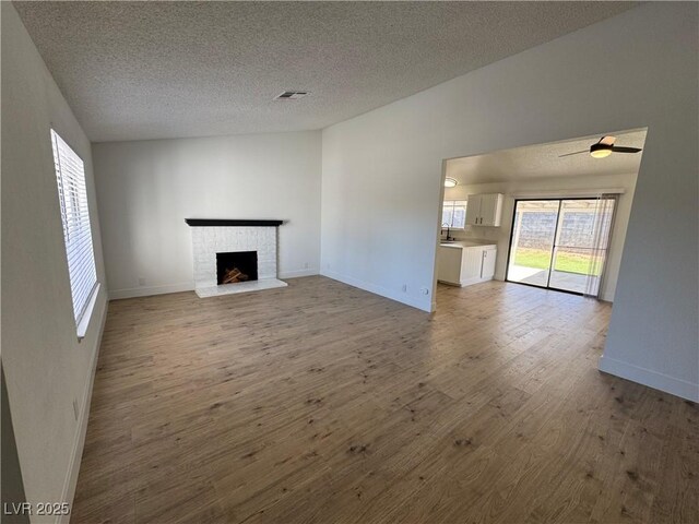 unfurnished living room with a fireplace, hardwood / wood-style flooring, a textured ceiling, and vaulted ceiling