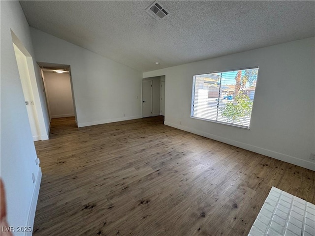 empty room with a textured ceiling, lofted ceiling, and hardwood / wood-style floors