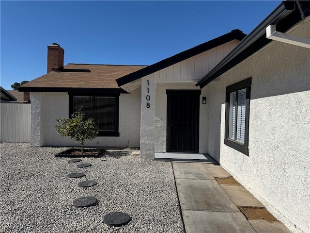 doorway to property with a shingled roof, fence, and stucco siding