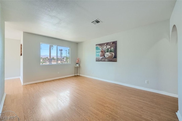 unfurnished room with arched walkways, a textured ceiling, visible vents, baseboards, and light wood-type flooring