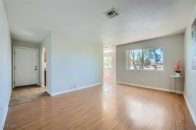 unfurnished room featuring arched walkways, visible vents, a textured ceiling, and light wood finished floors