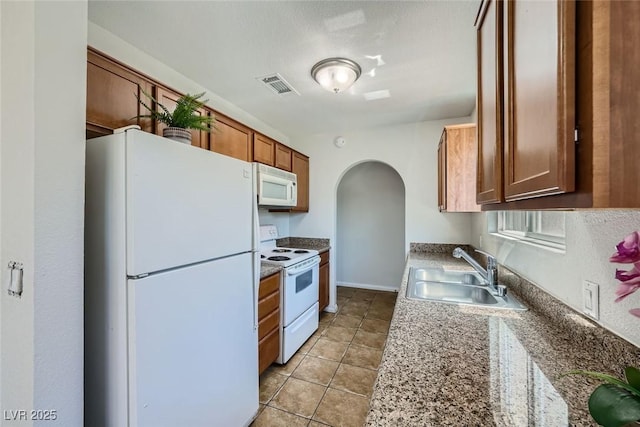 kitchen with white appliances, arched walkways, visible vents, brown cabinets, and a sink