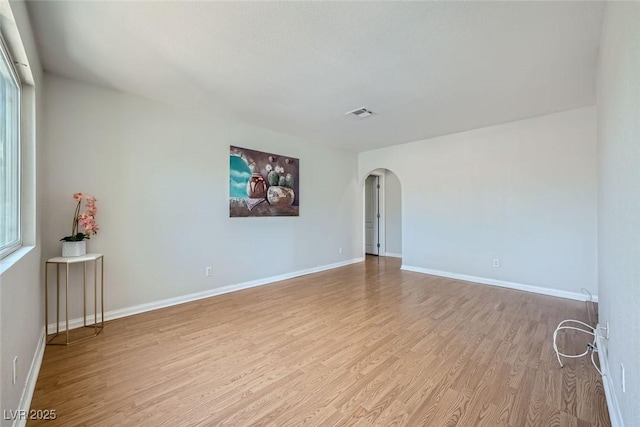 spare room with plenty of natural light, visible vents, arched walkways, baseboards, and light wood-style flooring