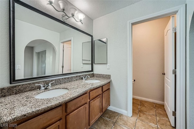 bathroom featuring a sink, a textured ceiling, baseboards, and double vanity