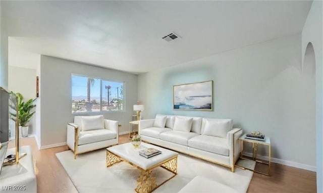 living area featuring light wood-type flooring, visible vents, arched walkways, and baseboards