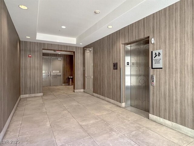 corridor with a raised ceiling, light tile patterned flooring, and elevator