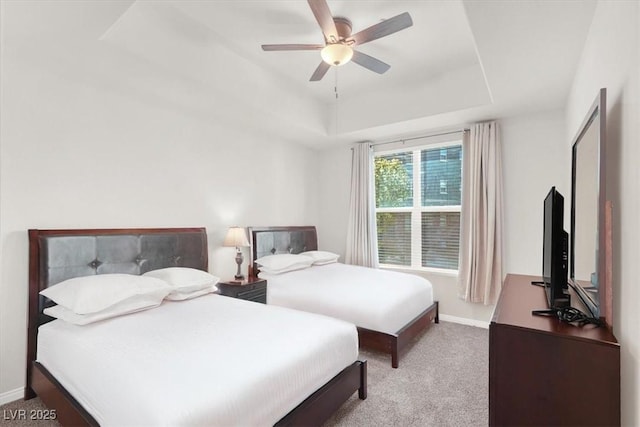 bedroom featuring ceiling fan, a tray ceiling, and light carpet