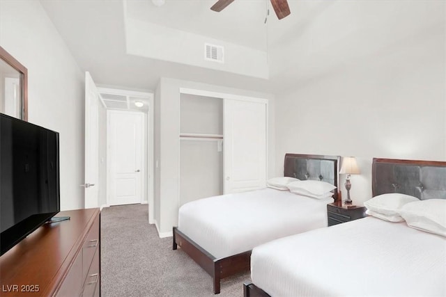 carpeted bedroom featuring a raised ceiling, ceiling fan, and a closet