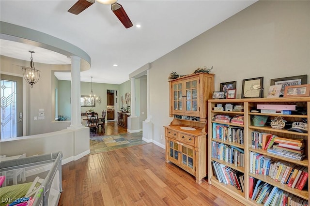 living area with ceiling fan with notable chandelier, light hardwood / wood-style floors, and ornate columns