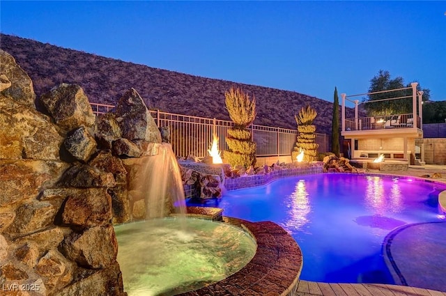 view of pool with a fire pit, fence, and a pool with connected hot tub