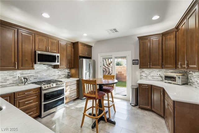 kitchen with decorative backsplash, appliances with stainless steel finishes, a kitchen bar, and dark brown cabinets