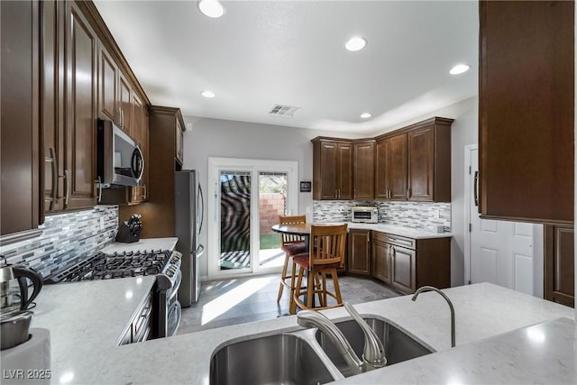 kitchen with sink, decorative backsplash, light stone counters, dark brown cabinetry, and stainless steel appliances