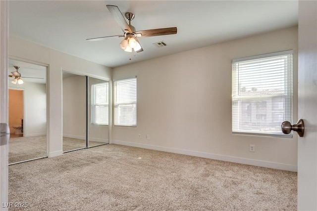 unfurnished bedroom featuring light carpet, ceiling fan, and multiple closets