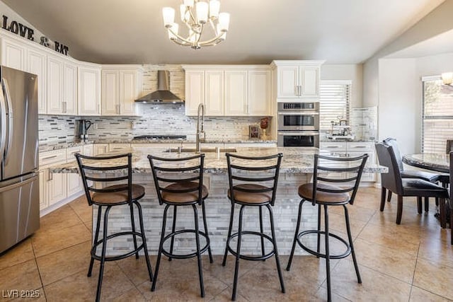 kitchen featuring hanging light fixtures, stainless steel appliances, light stone countertops, an inviting chandelier, and wall chimney exhaust hood