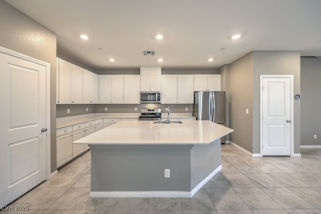 kitchen featuring sink, light tile patterned floors, appliances with stainless steel finishes, a kitchen island with sink, and white cabinetry