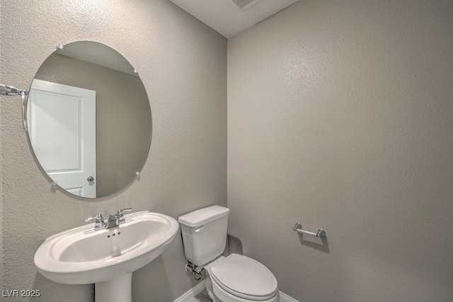 half bath featuring toilet, baseboards, a sink, and a textured wall