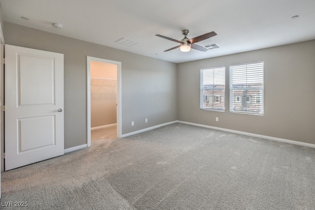 unfurnished bedroom with a walk in closet, light colored carpet, ceiling fan, and a closet