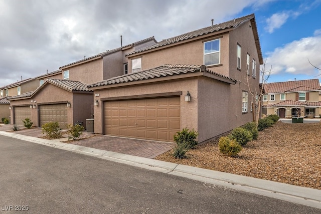 mediterranean / spanish home with an attached garage, a tiled roof, decorative driveway, and stucco siding