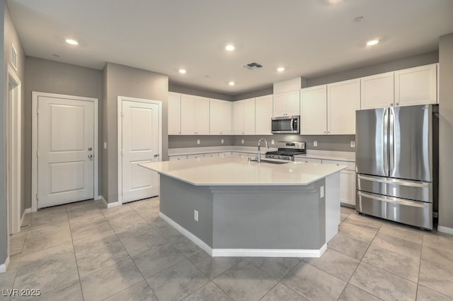 kitchen with appliances with stainless steel finishes, white cabinetry, an island with sink, sink, and light tile patterned floors