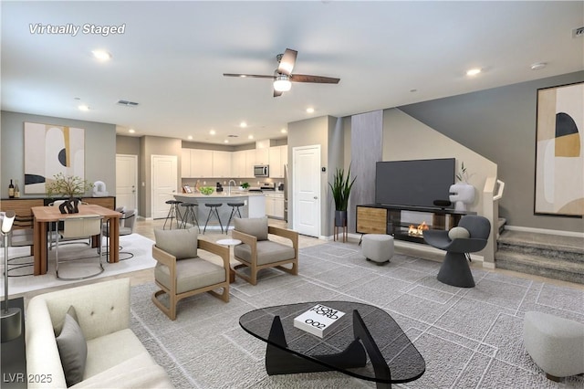 living area featuring recessed lighting, a ceiling fan, baseboards, visible vents, and a glass covered fireplace