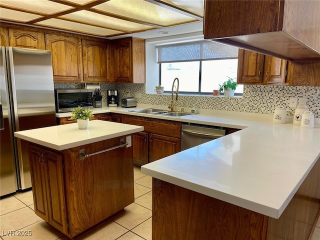 kitchen with stainless steel appliances, a peninsula, a sink, light tile patterned flooring, and backsplash