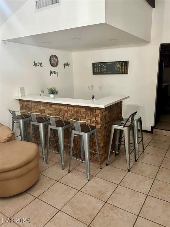 bar featuring wet bar, visible vents, a high ceiling, and light tile patterned floors