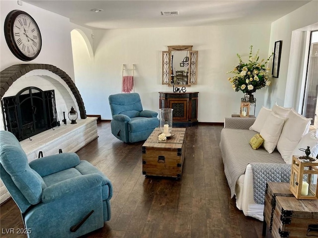 living room with baseboards, visible vents, a fireplace with raised hearth, and hardwood / wood-style floors