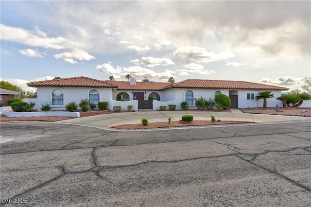 mediterranean / spanish home featuring stucco siding, a tile roof, and concrete driveway
